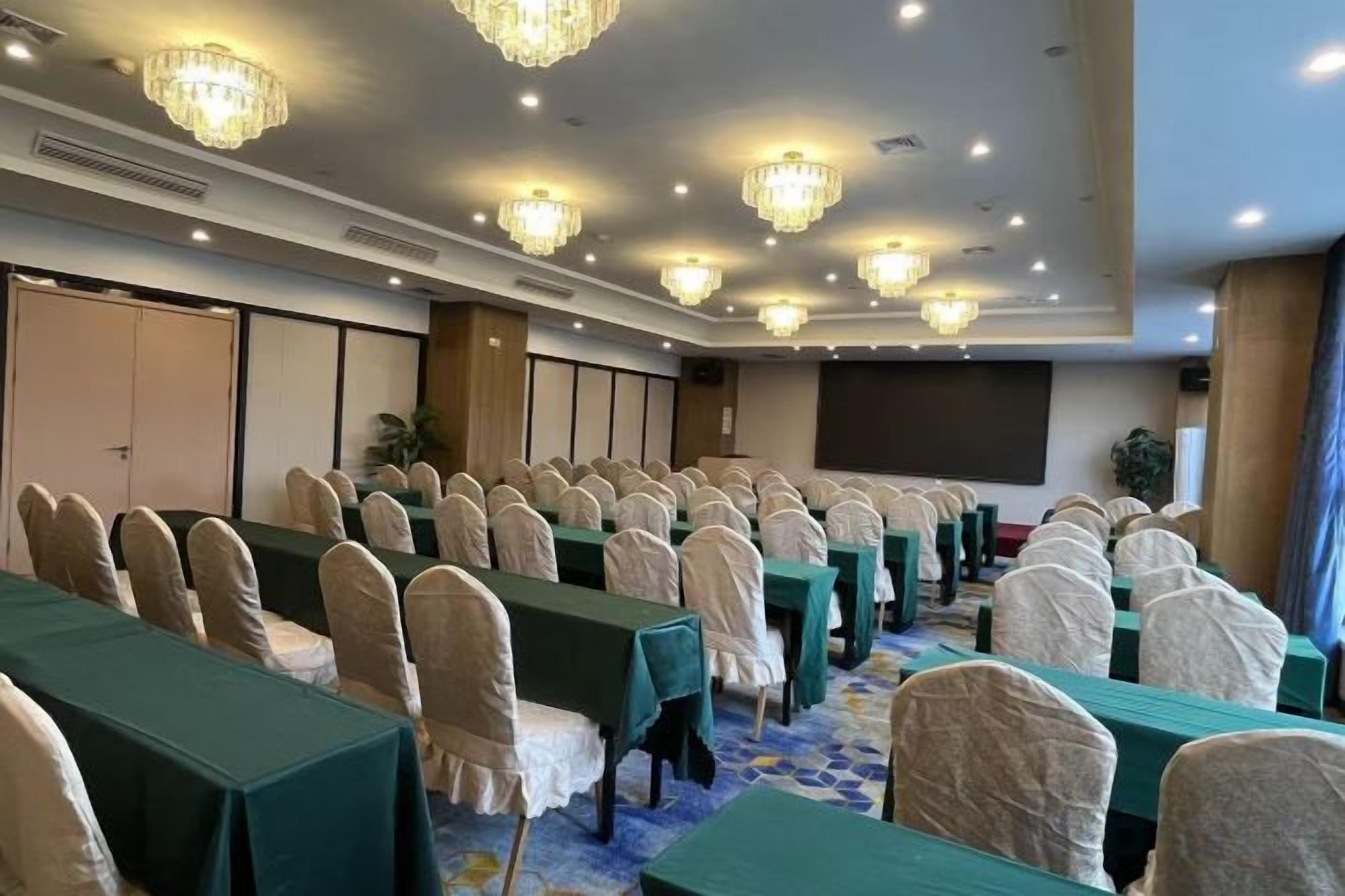 A conference room with rows of tables and chairs, a large screen, and chandeliers.