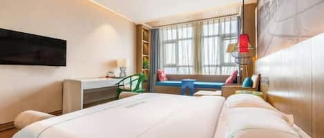 A hotel room with a large bed, a desk, a chair, a TV mounted on the wall, and a window with curtains.