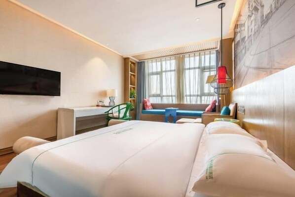 Une chambre d’hôtel avec un grand lit, un bureau, une chaise, un téléviseur fixé au mur et une fenêtre avec des rideaux.