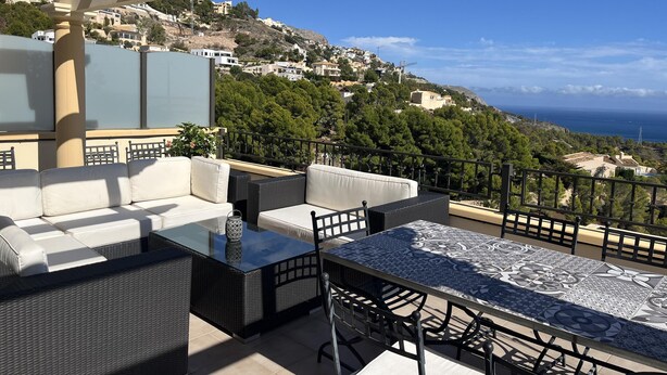 A terrace with outdoor furniture, a glass table, and a view of a hillside with buildings and the sea. - Altea Hills Hideaway With Stunning Views (Altea)