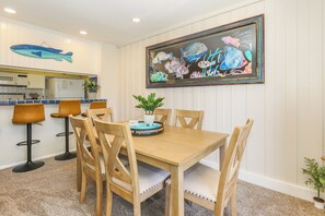 A dining area with a wooden table, four chairs, a potted plant, and a framed fish mural on the wall. - NCV C4 Beautiful beachfront cottage, all new furnishings w/ Stunning Ocean views (Oceanside)