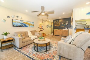 A living room with a sofa, armchair, coffee table, and a rug. There is a kitchen area with a microwave and a bar sign. - NCV C4 Beautiful beachfront cottage, all new furnishings w/ Stunning Ocean views (Oceanside)
