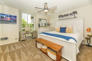 A bedroom with a bed, a desk, a chair, a bench, a ceiling fan, and a window with a view of palm trees. - NCV C4 Beautiful beachfront cottage, all new furnishings w/ Stunning Ocean views (Oceanside)