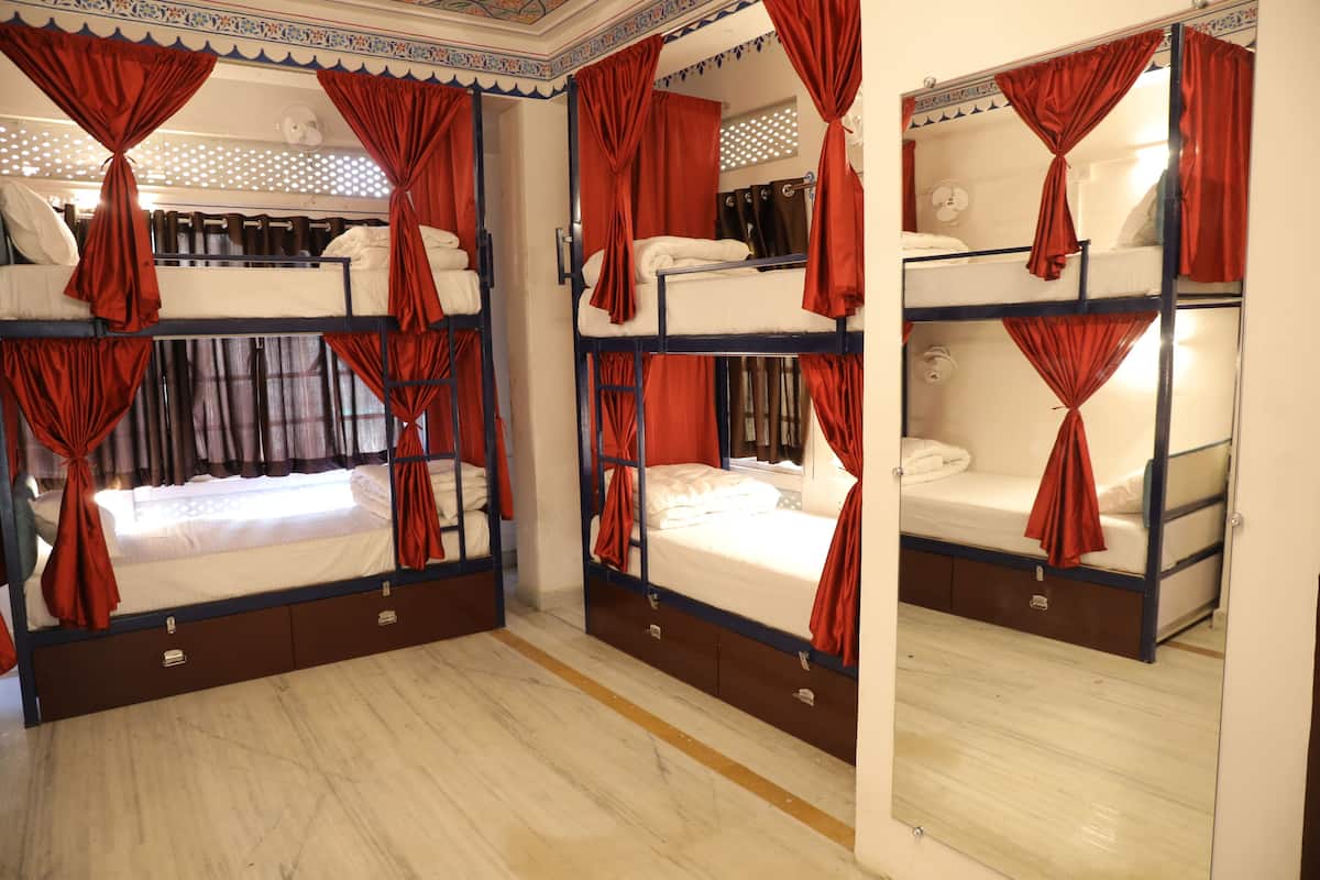 A room with bunk beds, each with a mattress and pillows, and red curtains.