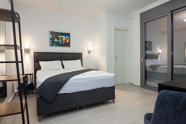 Ett modernt hotellrum med en stor säng, ett skrivbord och en stol. Det finns en tavla på väggen och en dörr som leder till ett annat rum.