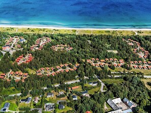 Una vista aerea di una zona residenziale costiera con case raggruppate, circondata da fitti boschi e una spiaggia sullo sfondo.