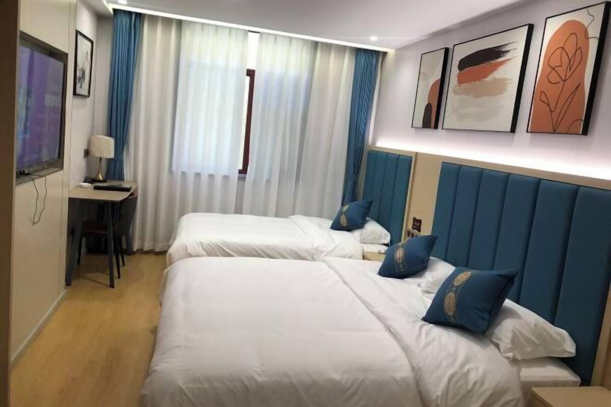 Ένα δωμάτιο ξενοδοχείου με δύο κρεβάτια, ένα γραφείο με ένα φωτιστικό, μια τηλεόραση και έργα τέχνης στον τοίχο.