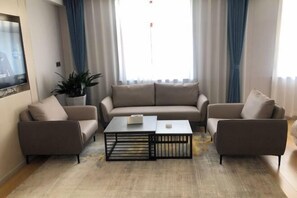 Una sala de estar con un sofá, dos sillones, una mesa de centro, un televisor y un ventanal con cortinas.