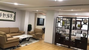 A modern living room with a sofa, armchair, coffee table, and a decorative cabinet with vases. - Zunhua GuestHotel (Zunhua)