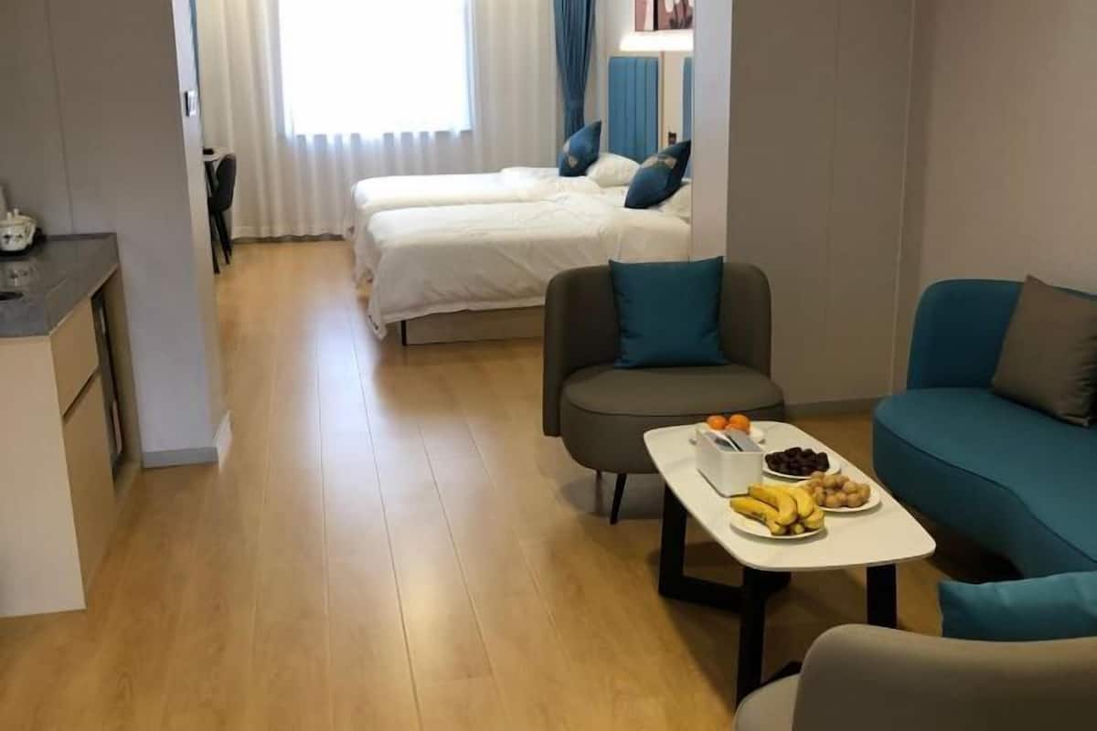 Ένα δωμάτιο ξενοδοχείου με δύο κρεβάτια, ένα τραπέζι φαγητού με φρούτα, έναν καναπέ και μια μικρή κου ζίνα.