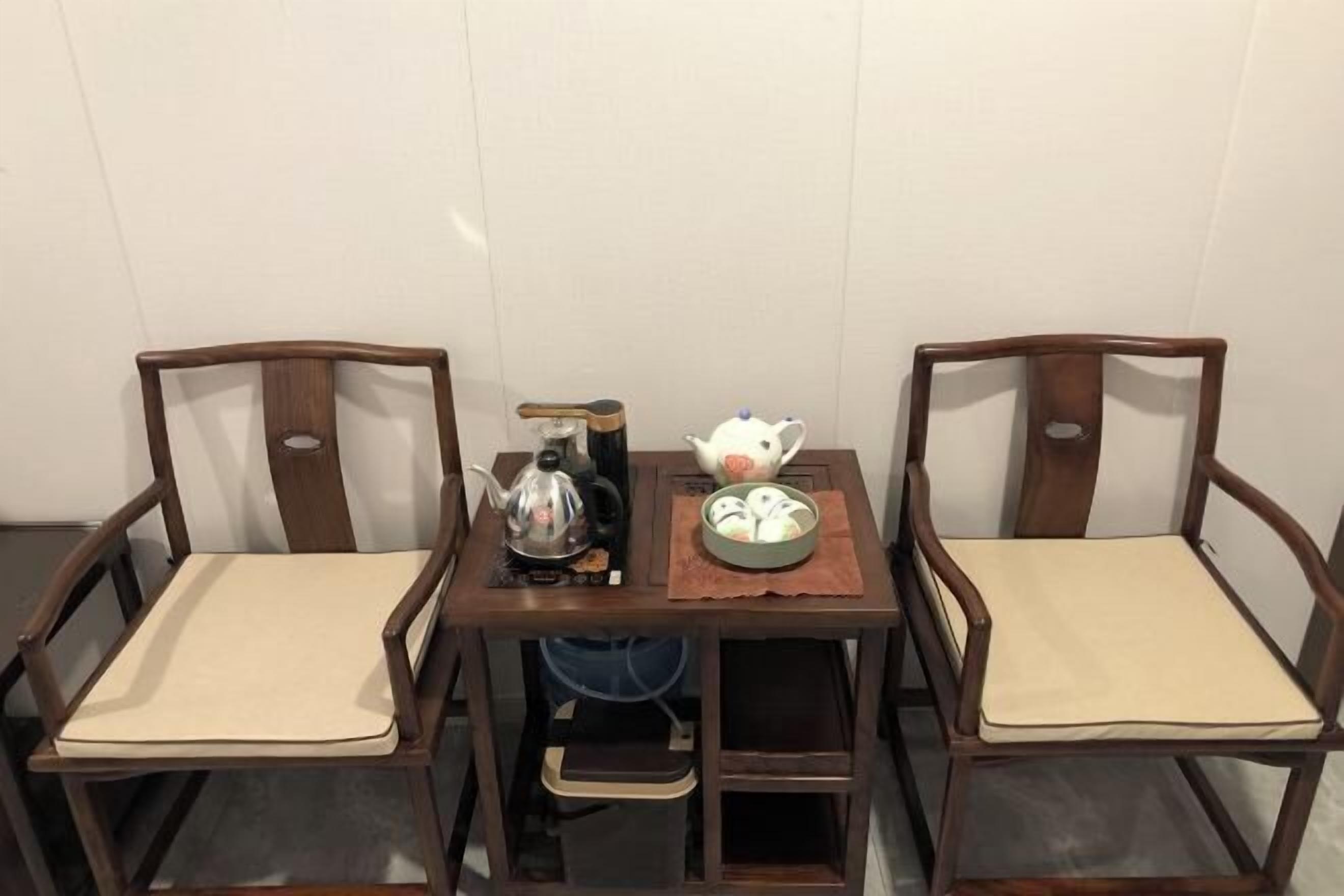 A dining table with two wooden chairs, a teapot, a kettle, and a bowl of fruit.