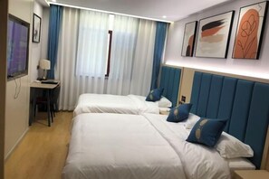 A hotel room with two beds, a desk with a lamp, a TV, and artwork on the wall. - Zunhua GuestHotel (Zunhua)
