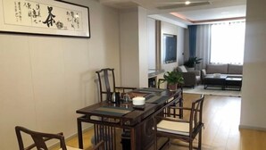 A dining area with a wooden table and chairs, a framed artwork on the wall, and a living room in the background. - Zunhua GuestHotel (Zunhua)