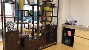 A room with a dark wooden cabinet with multiple shelves and drawers, a small table with decorative items, and a refrigerator on the right side. - Zunhua GuestHotel (Zunhua)