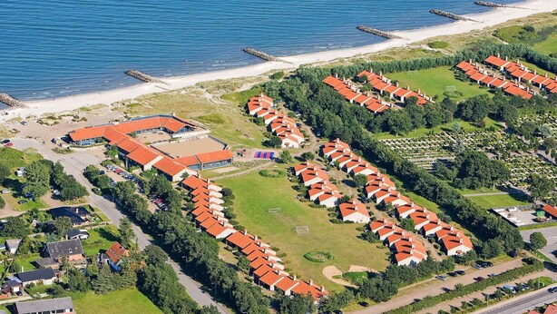 Ett flygbildsbild av en kustort med flera byggnader i bungalowstil, en sandstrand och en vågbrytare av sten.