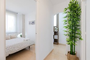 A bedroom with a bed, a window, a door, and a bamboo plant.