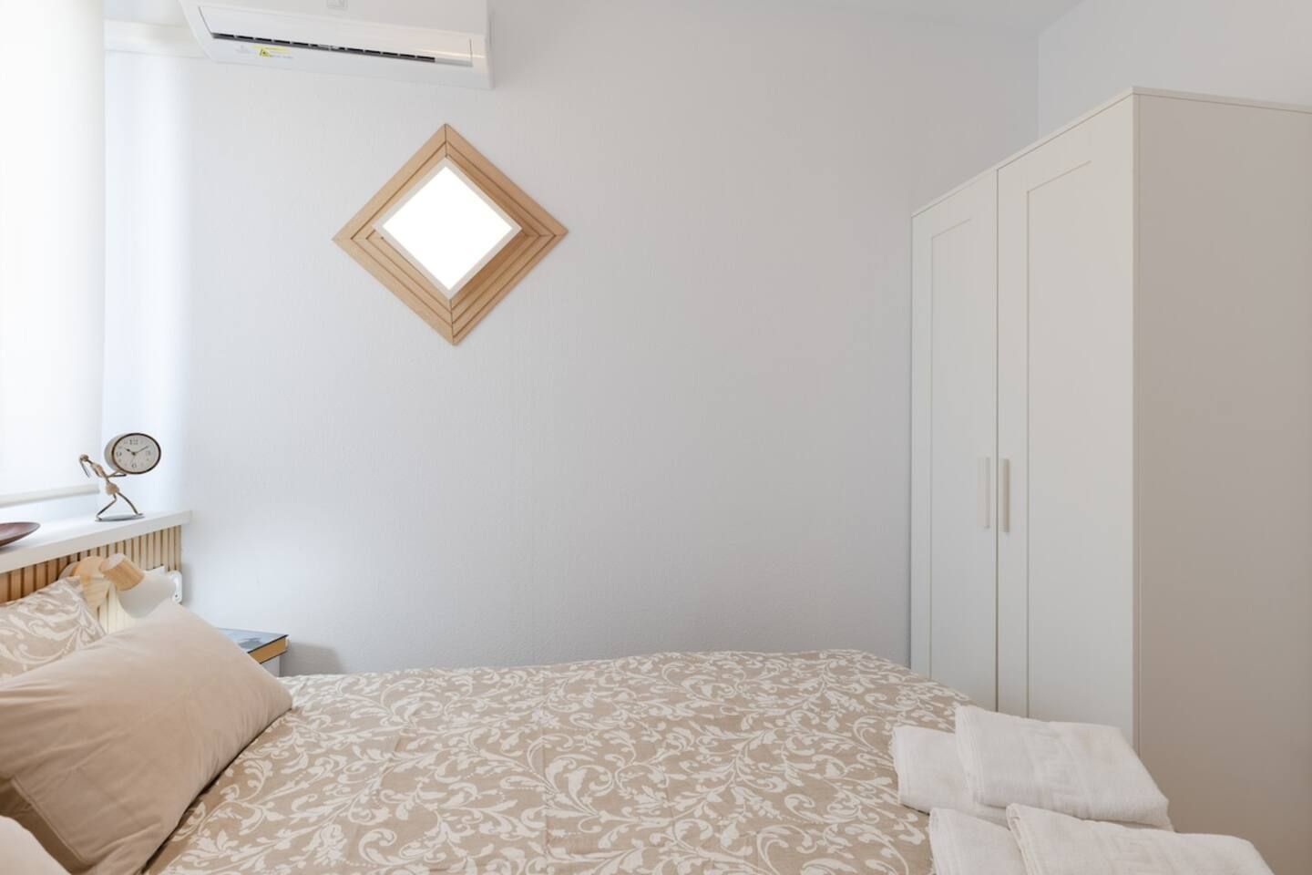 Une chambre à coucher avec un lit, une armoire, un radiateur, une horloge et une fenêtre.