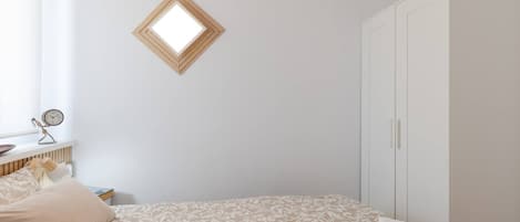 A bedroom with a bed, a wardrobe, a radiator, a clock, and a window.