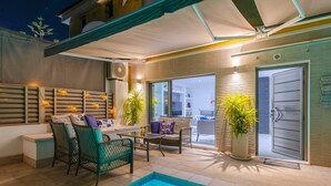 Un espace extérieur avec piscine, comprenant un coin salon couvert, une piscine et une porte donnant accès au bâtiment.