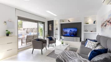 Een moderne woonkamer met een flatscreen televisie, grijze banken en een groot raam.