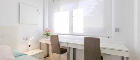 Un dormitorio moderno y bien iluminado con cama, escritorio, dos sillas y ventana que proporciona luz natural.