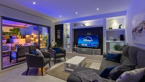 Un salon moderne doté d’un téléviseur à écran plat diffusant Disney+, d’un canapé, d’une table basse et d’un coin salon avec une porte vitrée donnant sur un espace extérieur.