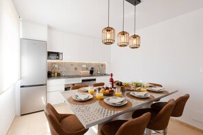 Eine moderne Küche mit weißen Schränken, einem Edelstahlkühlschrank und einem Essbereich mit gemustertem Tischlein.