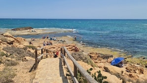Une plage côtière avec une promenade en bois menant à l’eau, un terrain rocheux et des gens qui profitent de la plage.