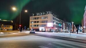 A multi-story building with a modern design, located at a city intersection with visible traffic lights and street signs. - Royal Roi Luxury suite (Rovaniemi)