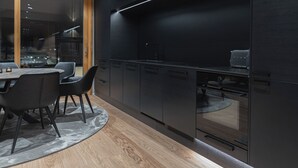 A modern kitchen with dark cabinetry, a built-in oven, and a dining area with a round table and chairs. - Royal Roi Luxury suite (Rovaniemi)