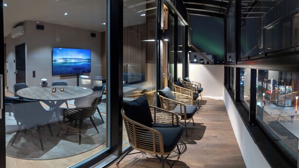 A modern conference room with a round table, chairs, a large flat-screen TV, and a glass wall offering a view of the cityscape. - Royal Roi Luxury suite (Rovaniemi)