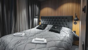 A modern bedroom with a tufted headboard, a grey quilted bedspread, two black pillows, and a pair of folded towels. - Royal Roi Luxury suite (Rovaniemi)