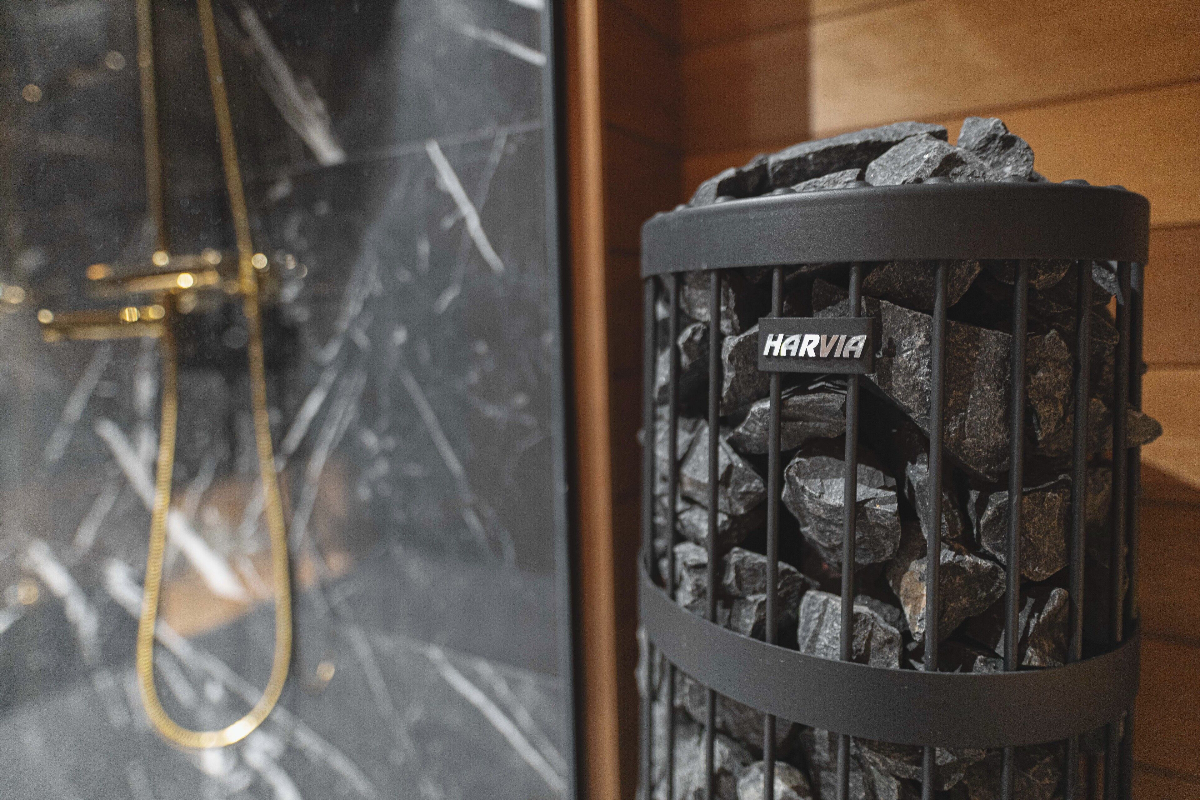 A fireplace with a metal grate labeled "HARVIA" and a gold-colored shower hose visible in the background.
