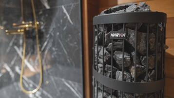 A fireplace with a metal grate labeled "HARVIA" and a gold-colored shower hose visible in the background.