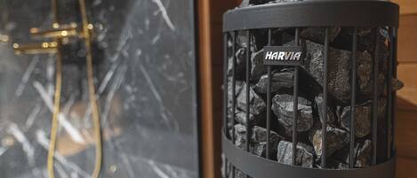 A fireplace with a metal grate labeled "HARVIA" and a gold-colored shower hose visible in the background.