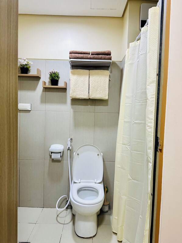 A small bathroom with a toilet, a shower curtain, and a towel rack with towels.