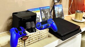A gaming setup with a PS4 console, a blue controller, and a microphone on a desk.