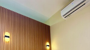A hotel room with a wooden headboard, a bed with white linens, two bedside lamps, and an air conditioning unit.