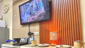 A modern living room with a flat-screen TV displaying a game, a coffee table with plates and a mug, and a wall-mounted lamp.