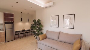 A modern living room with a sofa, a dining area with chairs, a large plant, and artwork on the wall. - Chill Out Apartments (Chania)