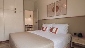A neatly made bed with white and red bedding, a bedside table with a lamp, and a wall-mounted artwork. - Chill Out Apartments (Chania)