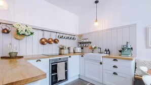 A modern kitchen with white cabinetry, a wooden countertop, and a hanging pot rack. - Rufloreo Dale (Derbyshire)