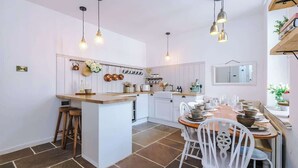 A kitchen with white cabinets, a central island, hanging lights, and a dining area with white chairs. - Rufloreo Dale (Derbyshire)