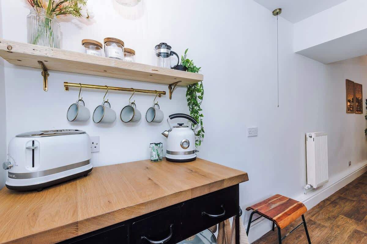 Una cucina con un piano di lavoro in legno, un tostapane, un bollitore e pentole appese.