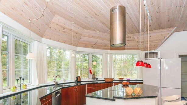 Una cucina moderna con un'isola grande, soffitto in legno e ampie finestre che danno su un panorama esterno.
