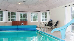 Una piscina interna con acqua cristallina, uno scivolo blu e una panchina in legno.
