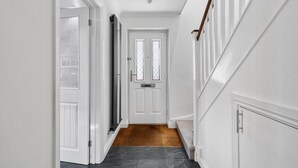 A hallway with white walls, a wooden staircase, and a door with a window. - Knights Rest - Minutes to the Port (Dover)