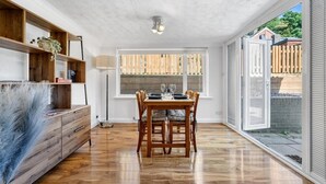 A dining area with a wooden table and chairs, a lamp, and a view of the outside through a window. - Knights Rest - Minutes to the Port (Dover)