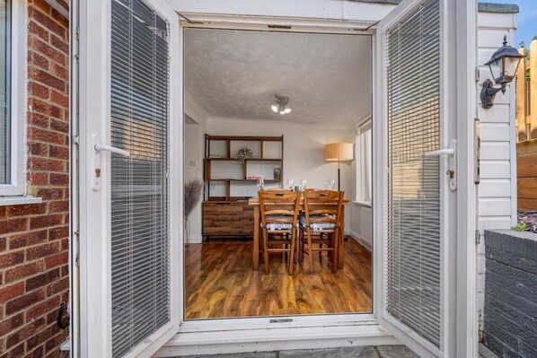 A dining area with a wooden table and chairs, a lamp, and a shelf with books. - Knights Rest - Minutes to the Port (Dover)