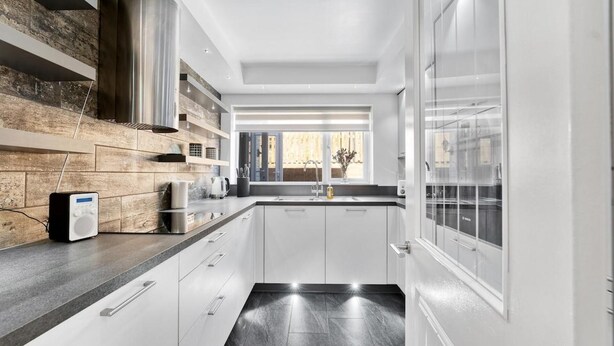 A modern kitchen with white cabinets, a wooden backsplash, and a window providing natural light. - Knights Rest - Minutes to the Port (Dover)